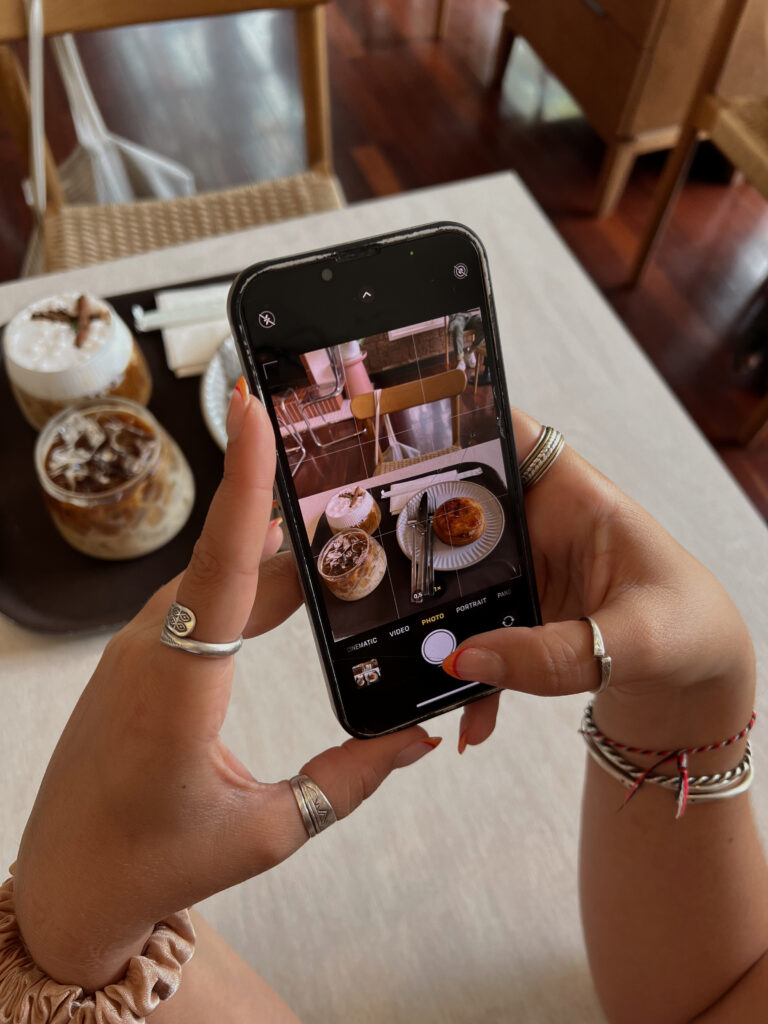 A guest takes a photo of their coffee and pastry at a café, capturing their experience on a smartphone.